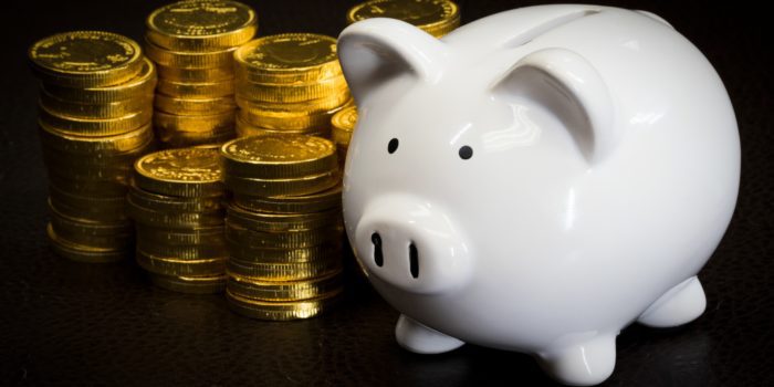 Piles of gold coins next to a white piggy bank
