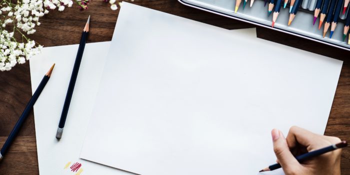 A hand holding a pencil at the corner of blank sheet of paper.