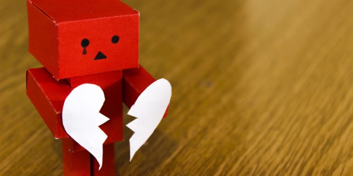 A little red robot holding a paper heart that's split in two.