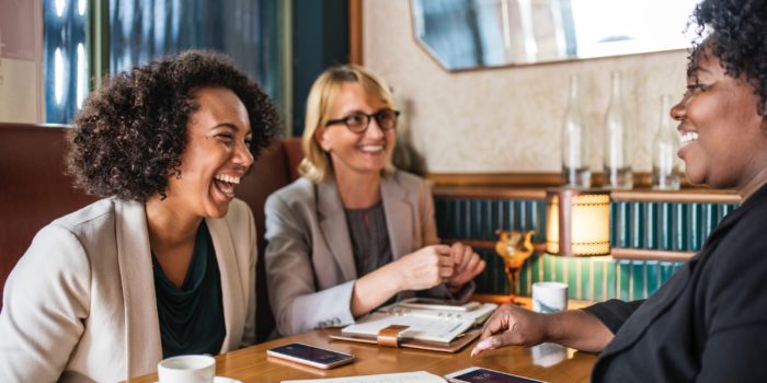 3 women, laughing and smiling, sitting round a table in a coffee shop.