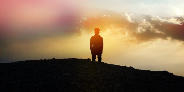 Silhouette of a person standing on a hill at sunset.